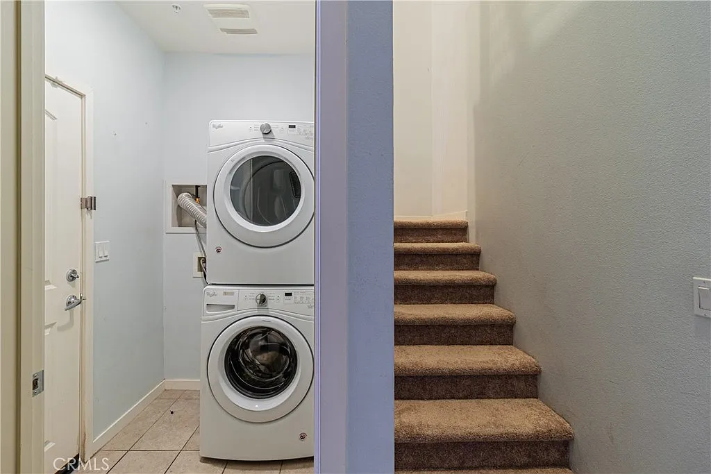 Laundry area with stacked washer and dryer and staircase on the right.