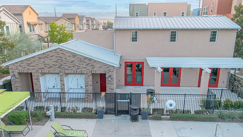 Aerial view of modern residential building with metal roof, red windows, fenced seating area, and surrounding houses.