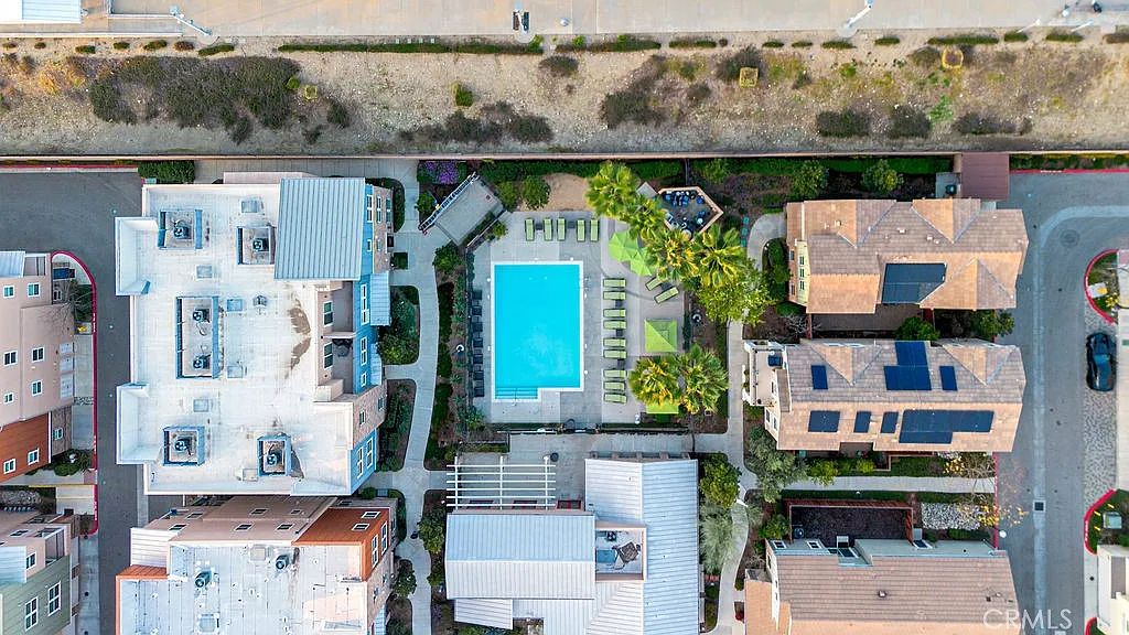 Aerial view of residential area with pool, lounge chairs, palm trees, and nearby buildings.