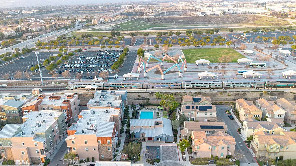 Aerial view of residential area with houses, parking lot, park, and train passing by.