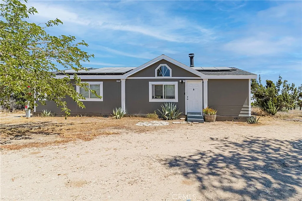 Single-story gray house with sloped roof, small porch, and desert landscape with sparse vegetation.