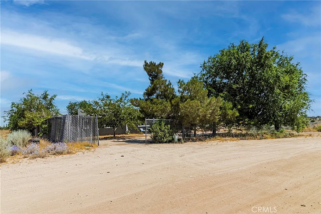 Sandy path leading to trees, fence, and structures