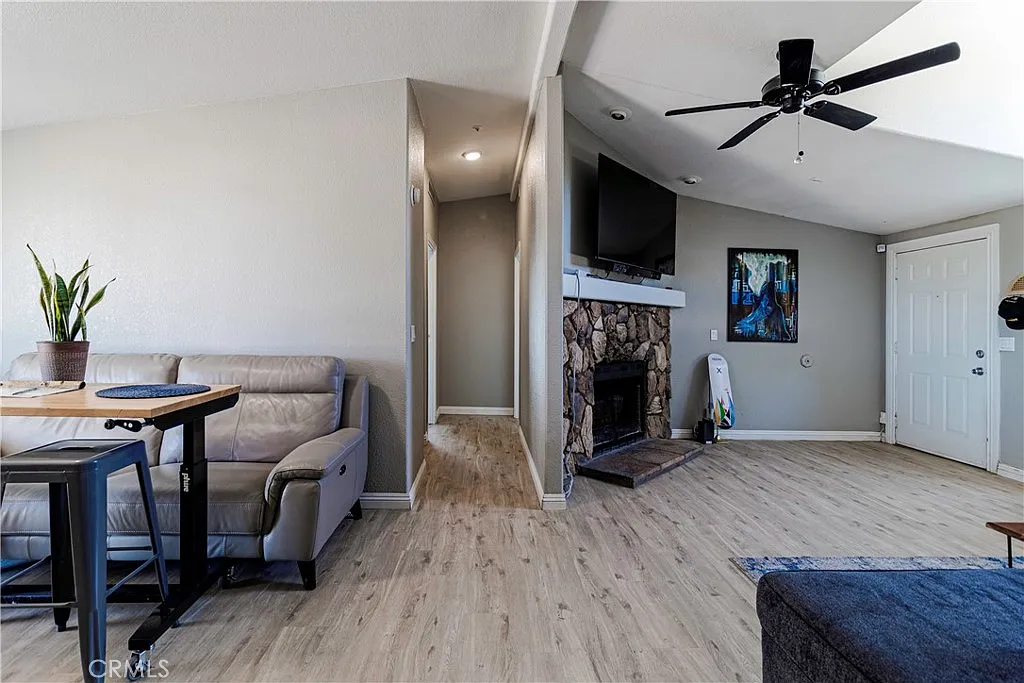 Living room with ceiling fan, stone fireplace, gray sofa, small dining table, and hallway with door.