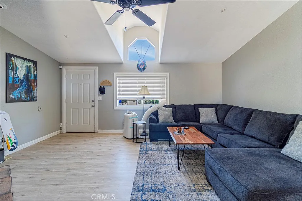 Living room with large dark sectional sofa, hardwood floor, window with blinds, coffee table, and wall artwork.