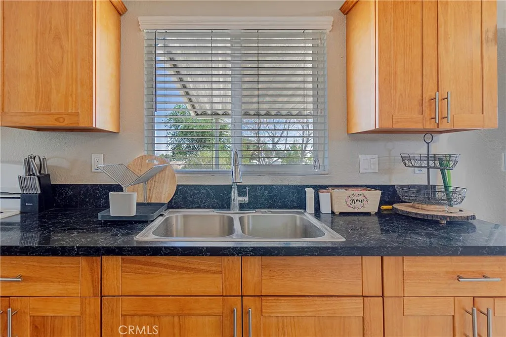 Kitchen with sink, window above, wooden cabinets, and black countertop.