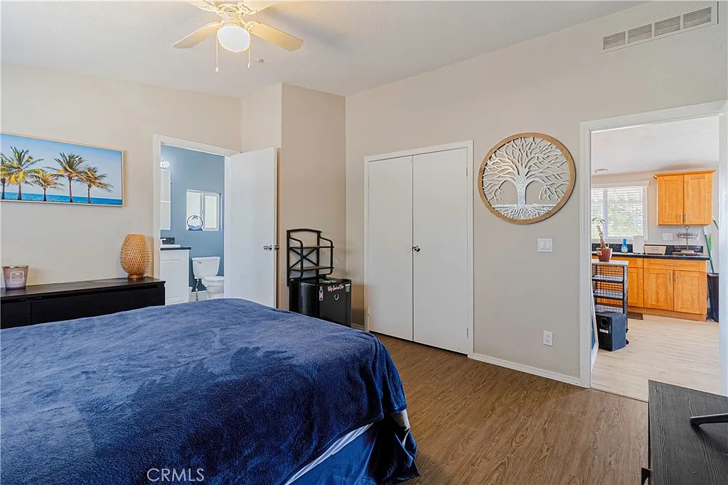 Bedroom with blue bedspread, ceiling fan, light walls, doorway, and visible bathroom.