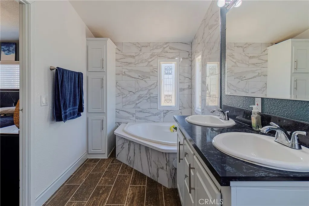 Modern bathroom with double sinks, marble walls, large bathtub, and window light.