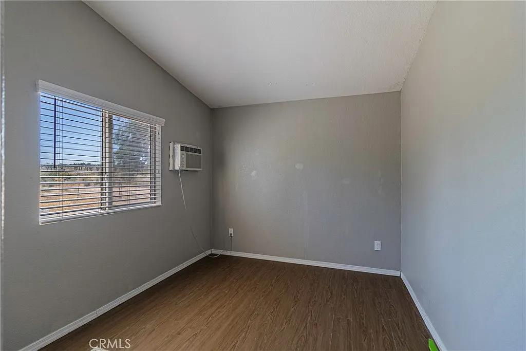 Room with gray walls, window with blinds, wooden floor, and air conditioning unit.