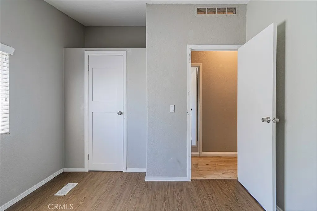 Room with gray walls, light wood floor, two doors, and window with blinds.