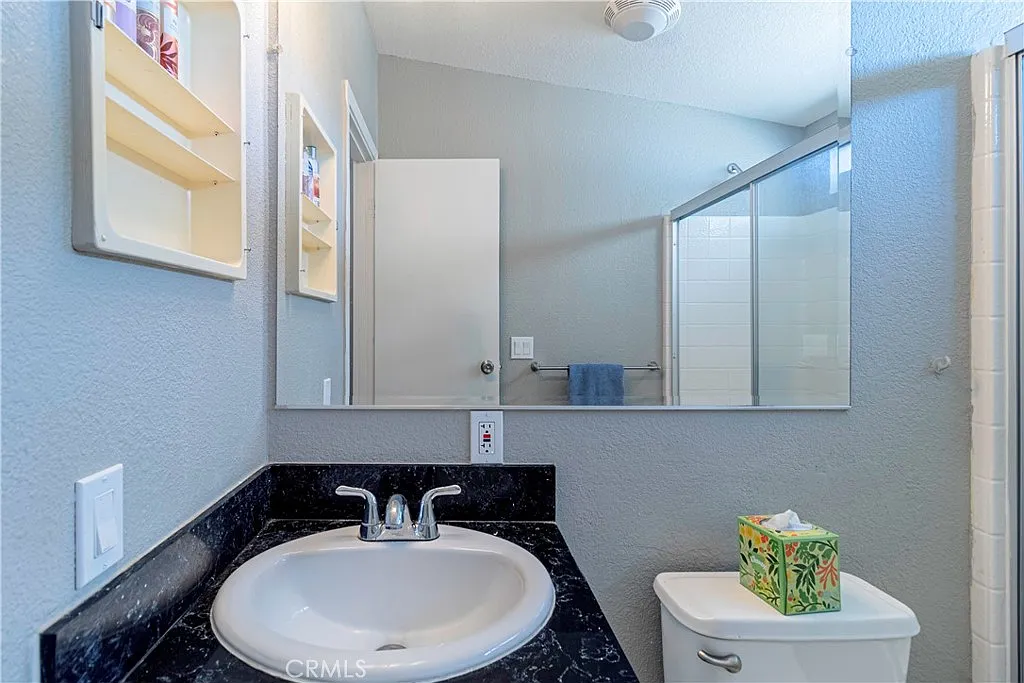 Bathroom with sink, mirror, toilet, shower, light gray walls, and tissue box on counter.