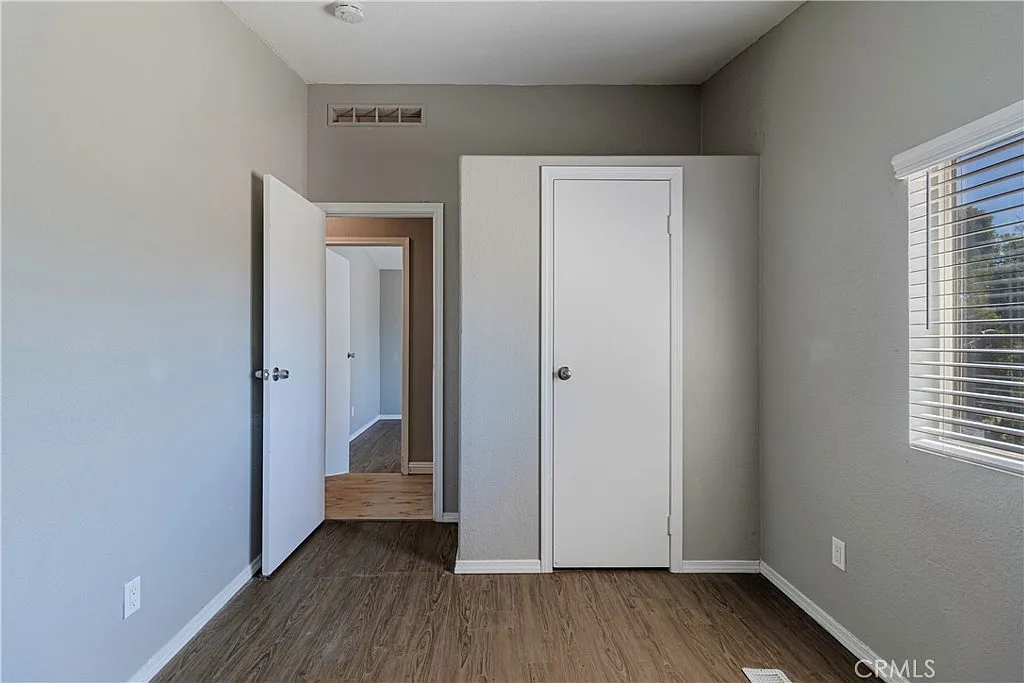 Room with gray walls, wooden floor, two doorways, and window with blinds.