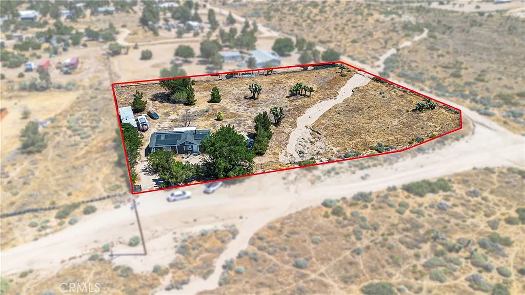 Aerial view of large land plot outlined in red with vegetation, house, and dry surroundings.