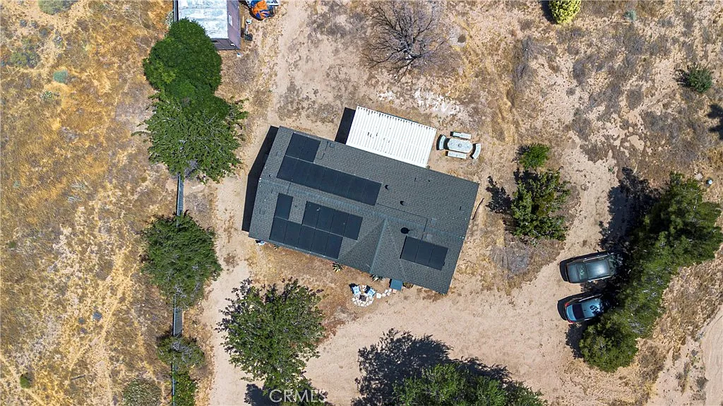 Aerial view of gray house with black roof, sparse vegetation, dirt, parked vehicles, and construction area.
