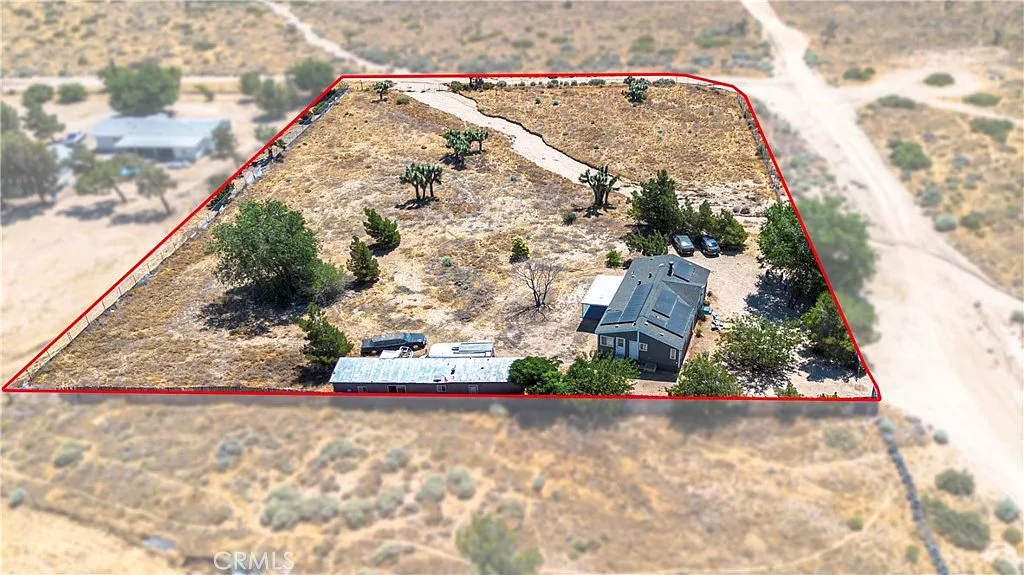 Aerial view of fenced property with sparse vegetation, paved path, house, and open land