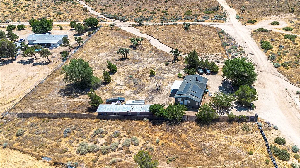 Aerial view of dry land with a house, open space, trees, and dirt paths.