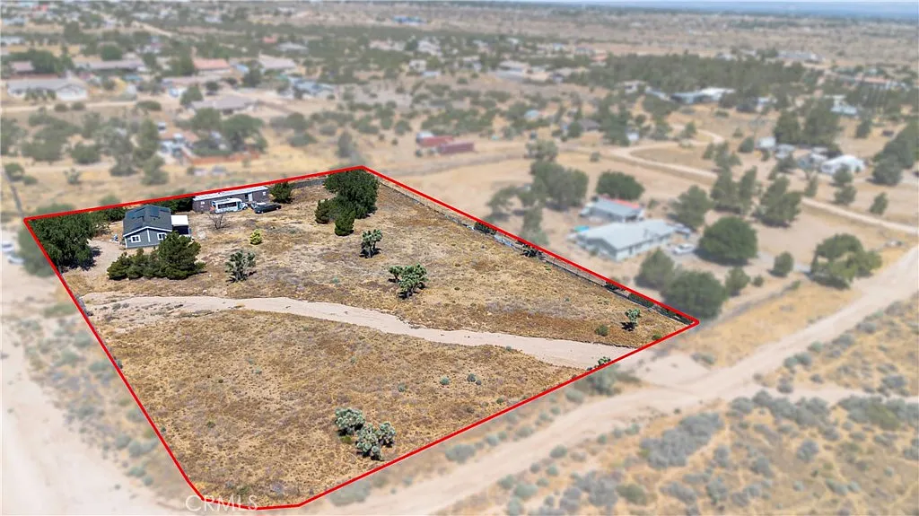 Aerial view of large land plot with sparse vegetation, central structures, and nearby houses.