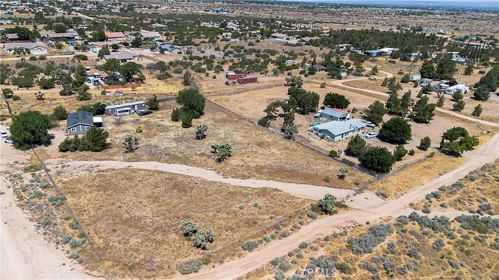 Aerial view of rural desert area with houses, sparse vegetation, and dirt roads.