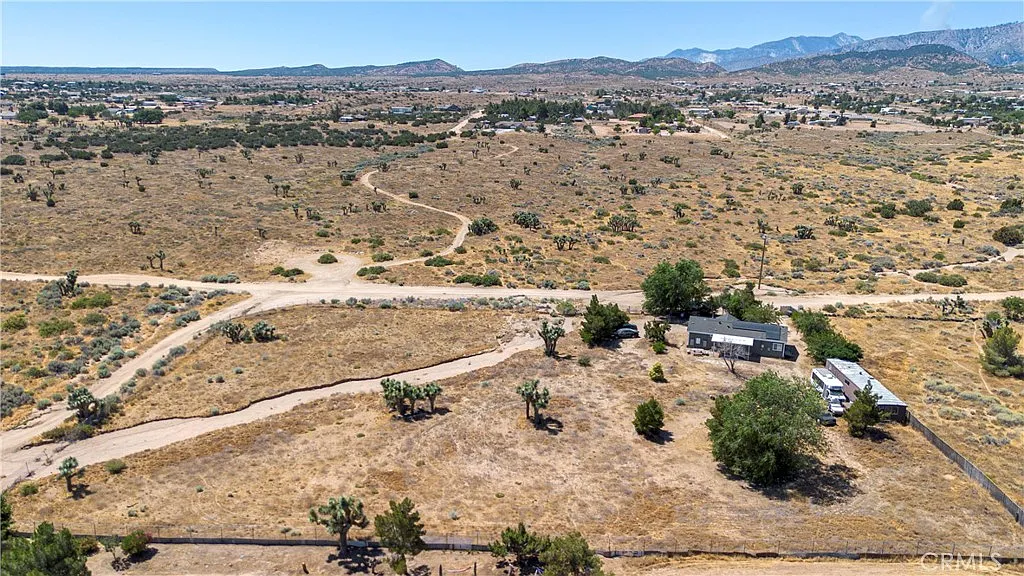 Aerial view of rural land with dirt roads, buildings, sparse plants, and mountains.