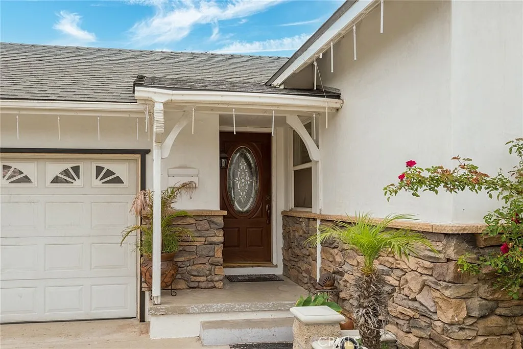 House entrance with wooden door, stone wall accents, flower bed, and garage door