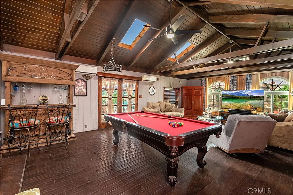Living room with billiards table, wooden ceiling beams, seating, large windows, decorative furniture, and bar area