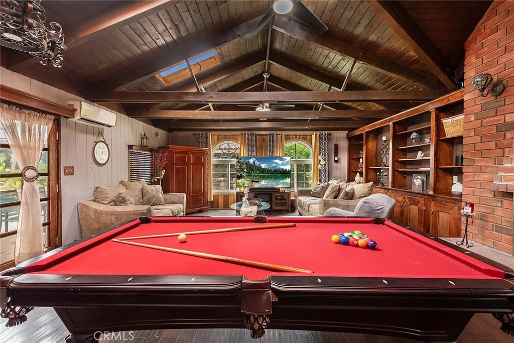 Living room with red pool table, wooden ceiling beams, large windows, and shelving units with items