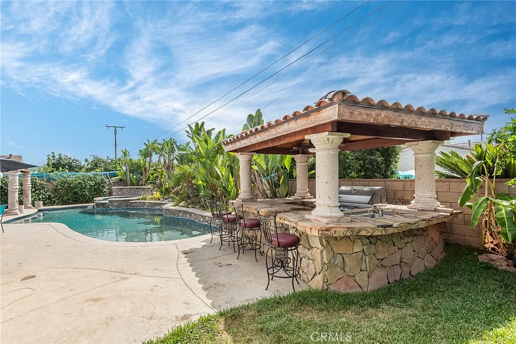 Backyard with swimming pool, outdoor bar with stools, and green plants