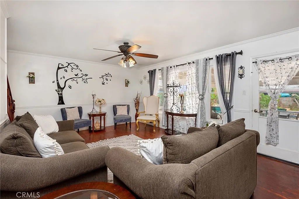 Living room with ceiling fan, brown sofas, chairs, table, wall art, and large windows with sheer curtains