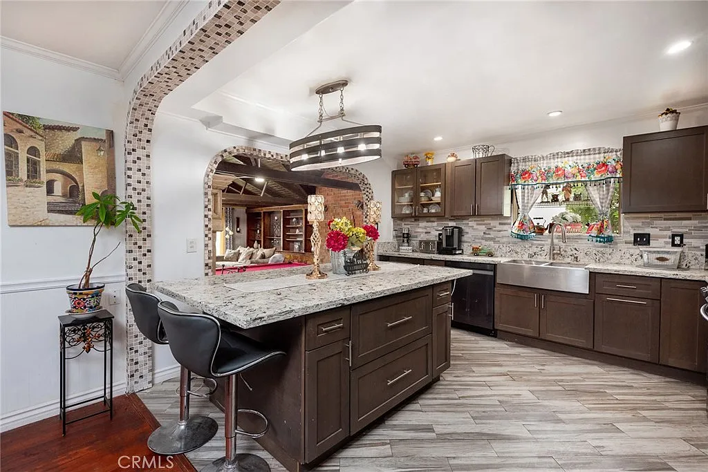 Kitchen with dark cabinets, large island with seating, granite countertops, colorful window, appliances, and decorative elements