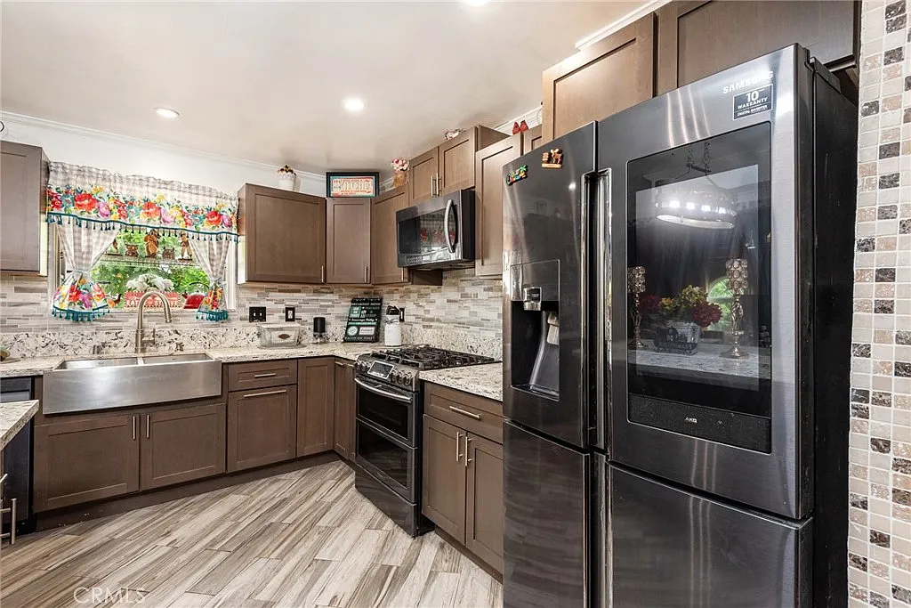Kitchen with dark cabinets, stainless steel appliances, quartz countertops, floral window treatment, and gray wood-like tile floor
