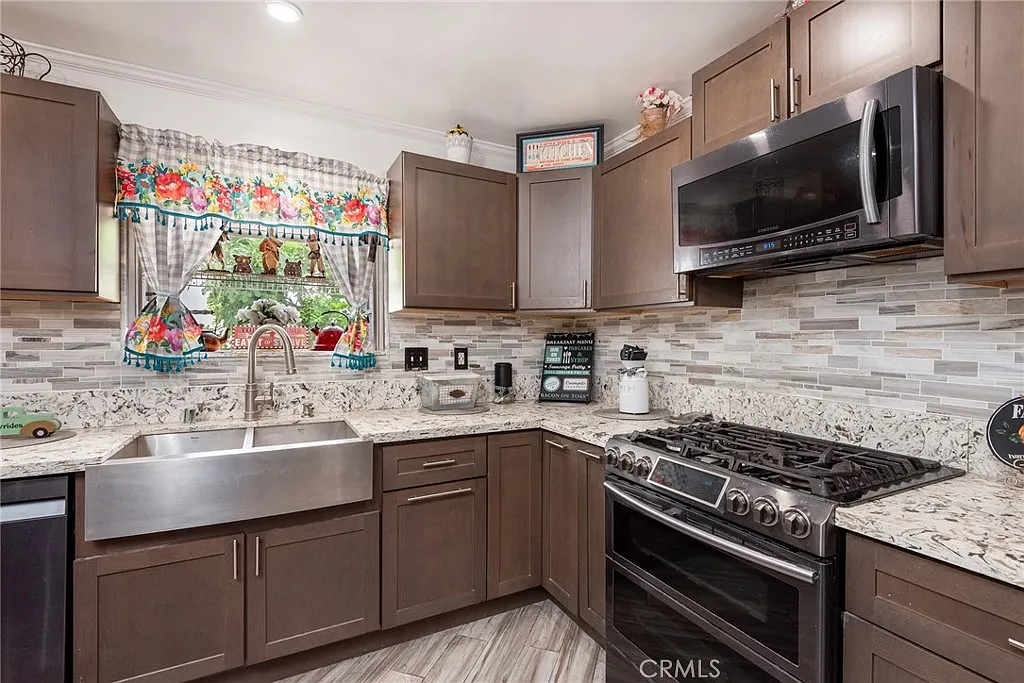 Kitchen with farmhouse sink, granite countertops, stainless steel appliances, wooden cabinets, and floral curtain