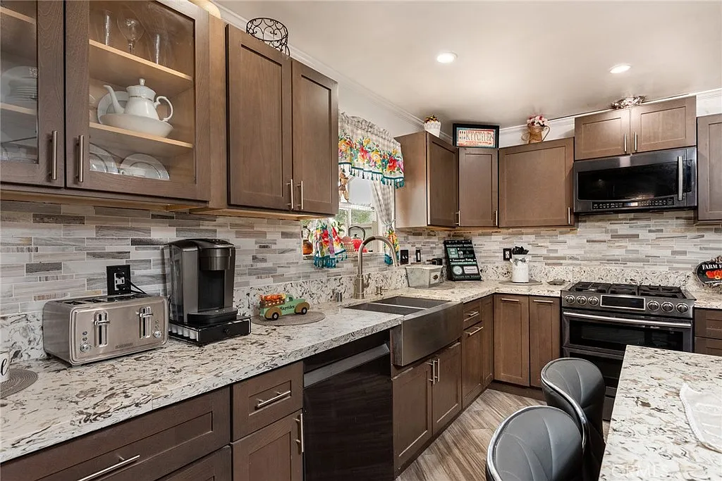 Kitchen with dark wood cabinets, granite countertops, stainless steel sink and appliances, decorative items, and colorful curtains