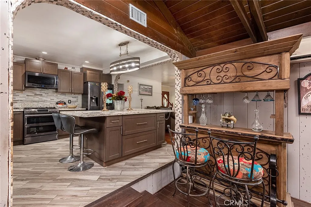 Modern kitchen with dark wood cabinets, stainless steel appliances, large island, and wooden bench with colorful cushions