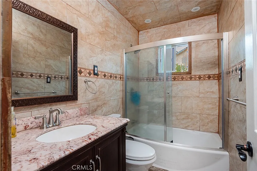 Bathroom with beige tiles, glass shower, white toilet, and sink with dark wood cabinets