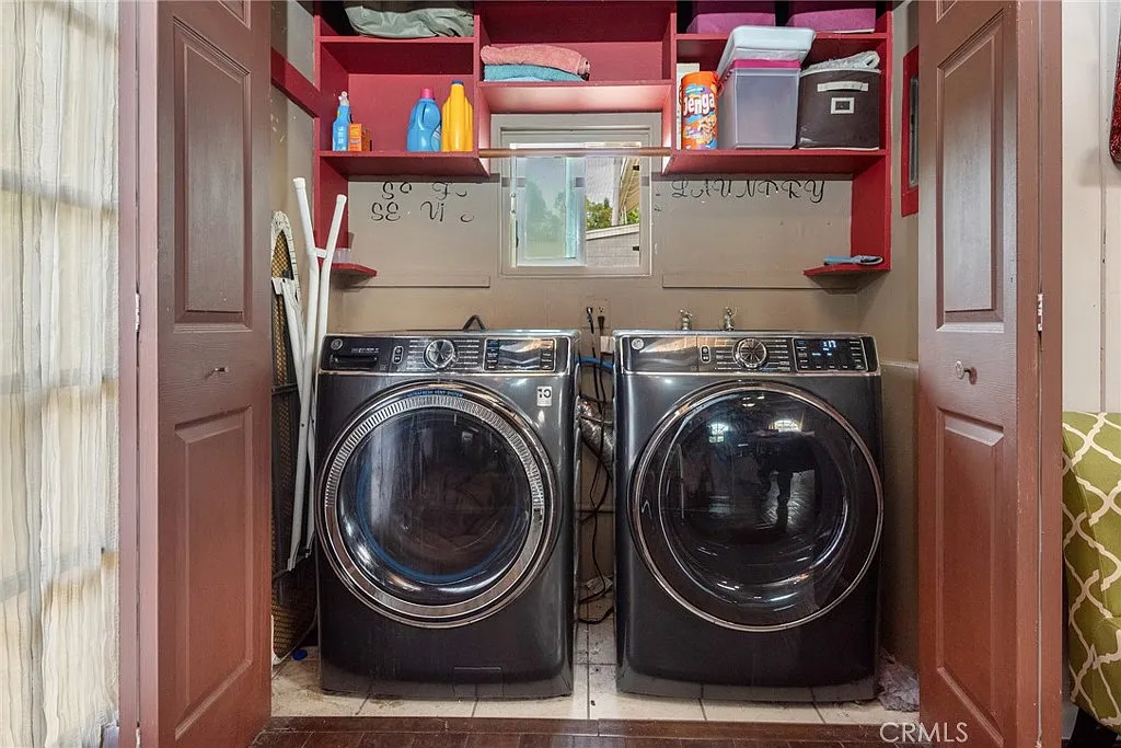 Laundry room with two black washing machines, shelves with supplies, brown doors, and window light