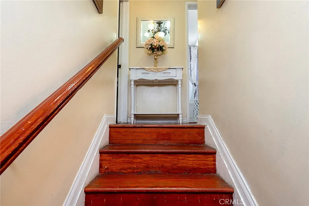 Staircase with wooden steps, white railing, small table with flowers, and light-colored walls