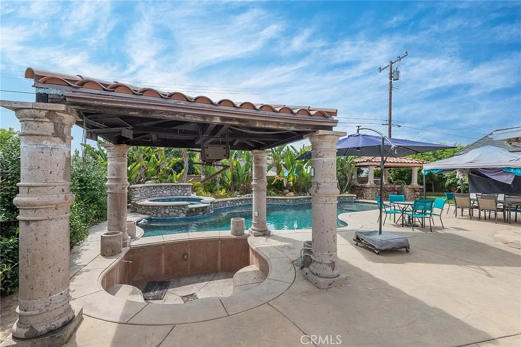 Landscaped outdoor area with pool, covered structure with columns, and seating arrangements