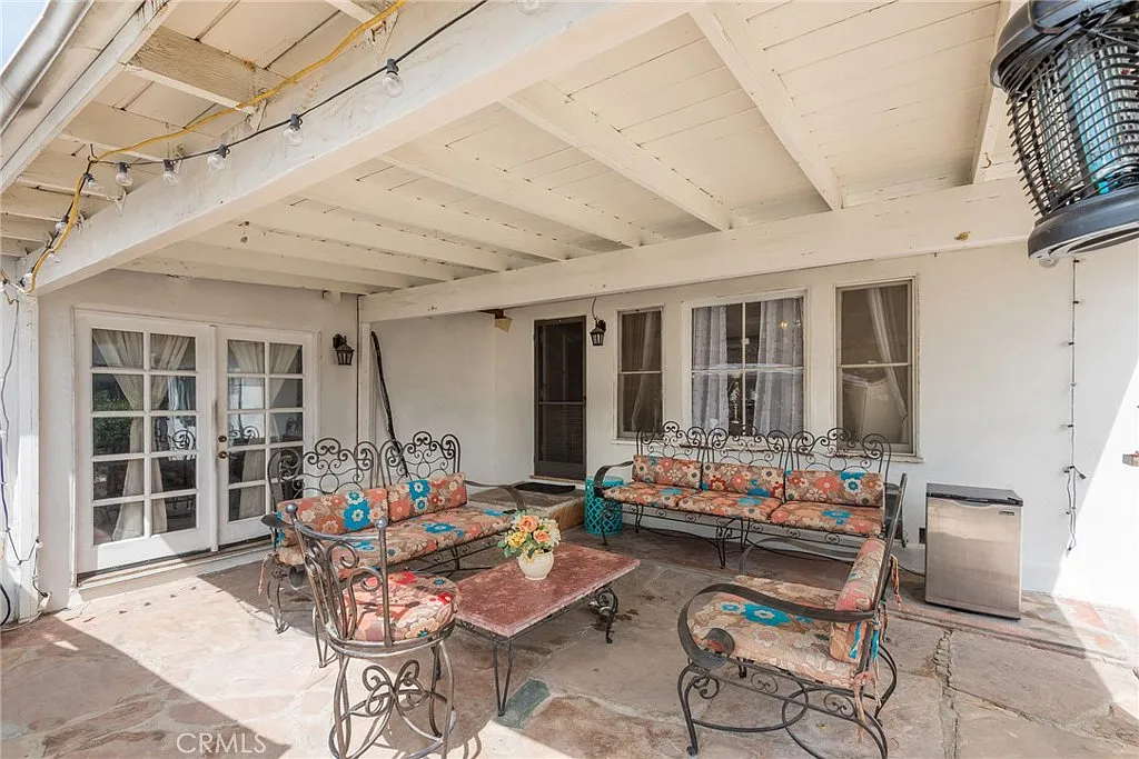 Covered patio with wrought iron furniture, colorful cushions, small table, lantern, and glass doors