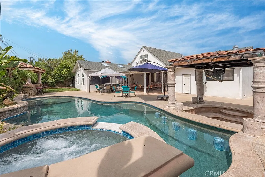 Backyard with swimming pool, spa, patio furniture, umbrellas, and white buildings with trees