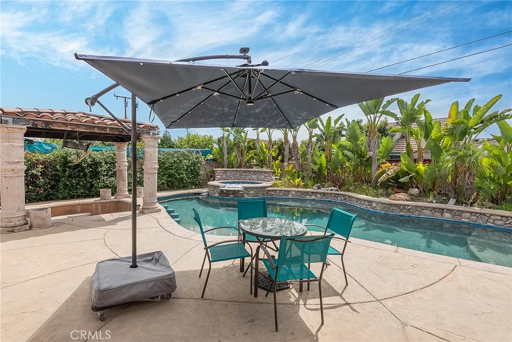 Patio with table and chairs under umbrella, next to swimming pool and tropical plants