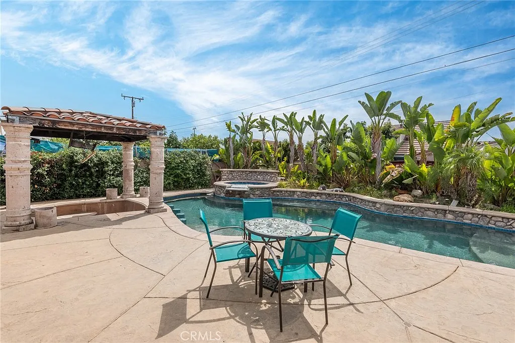 Pool area with stone patio, blue table and chairs, palm trees, and shrubs
