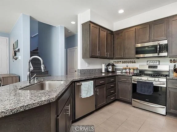 Modern kitchen with dark wood cabinets, granite countertops, stainless steel appliances, and sink