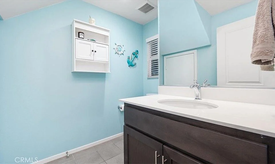 Bathroom with light blue walls, white wall shelf, mirror, and dark wooden vanity with sink