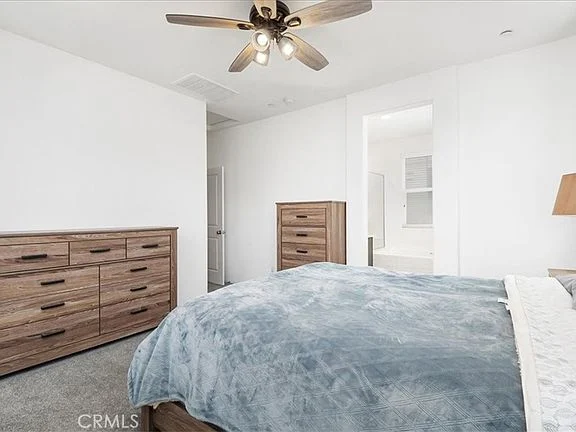 Bedroom with gray blanket, wooden dressers, ceiling fan, and white walls