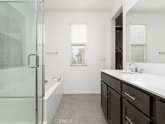 Bathroom with glass shower, bathtub, double vanity with dark cabinets, white counter tops, and windows with natural light
