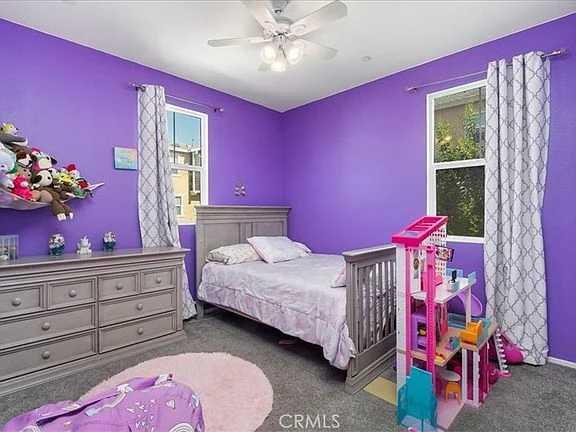 Children's bedroom with purple theme, bed, dresser, toy play set, plush toys, and bright natural light from windows