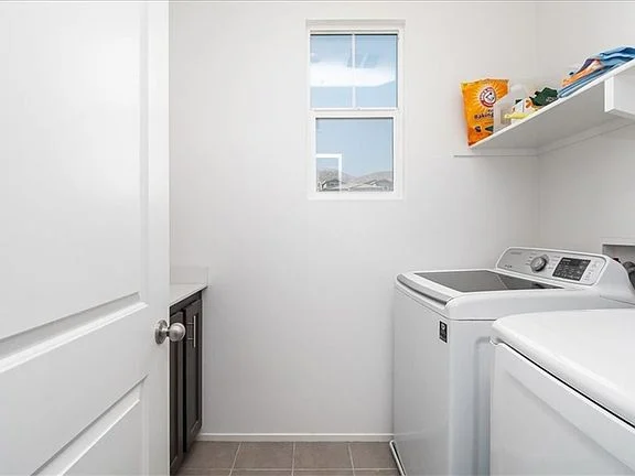 Laundry room with washing machine, dryer, window, shelves above, and gray tile floor