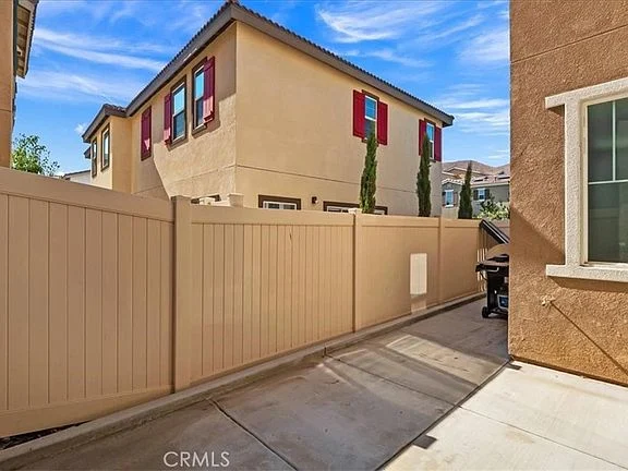 Narrow pathway between two buildings with tan fence and green shrubs