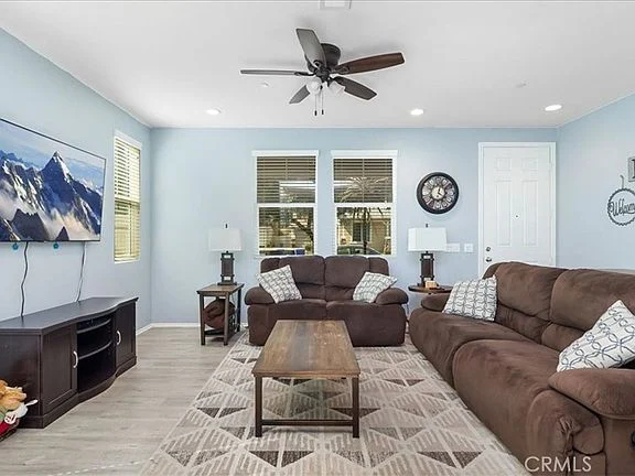 Living room with brown sofas, wooden coffee table, wall-mounted TV, two large windows, and light blue wall