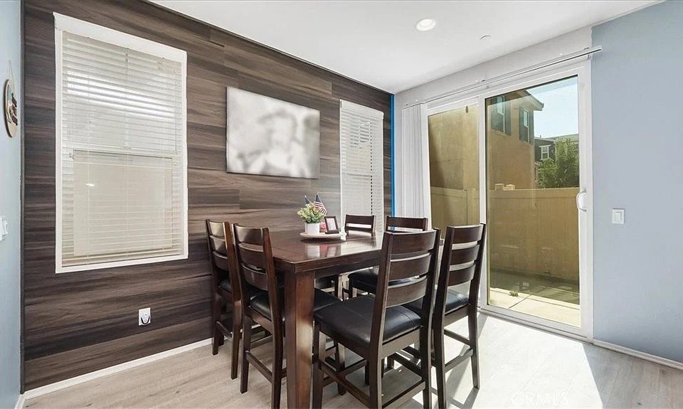 Dining area with wooden table and chairs, large windows, sliding glass door, wood-paneled walls, and framed picture