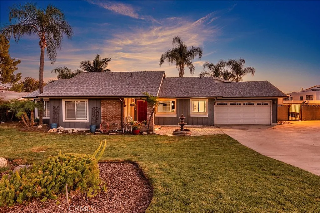 Single-story real estate house with gray roof, landscaped front yard, palm trees, small fountain, and driveway